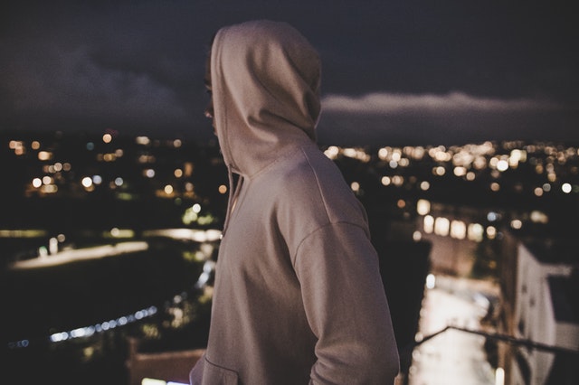 En ung fyr i hættetrøje, der står og kigger udover en oplyst by, om natten