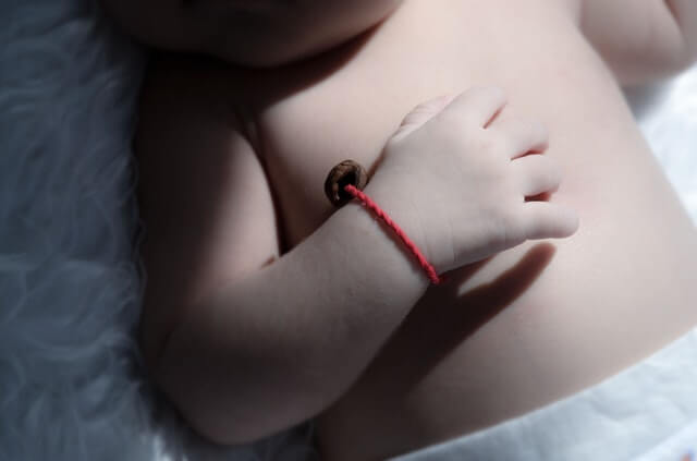 En mor der holder sit barn i hånden, som bærer et rødt armbånd med guld vedhæng i