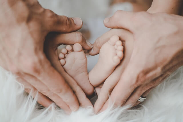 En far og en mor der holder om sit barns fødder og danner et hjerte